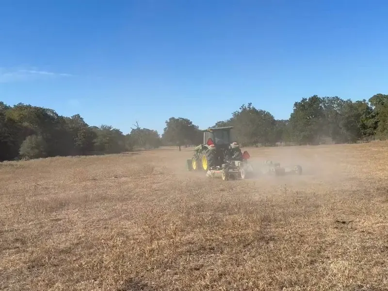 Tractor working an open dry pasture in a cloud of dust